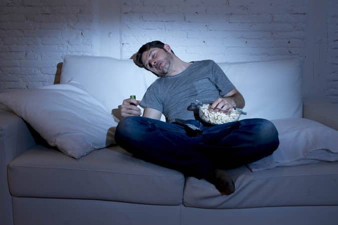 Man sleeping on a sofa with popcorn and a beer