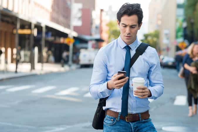 Man carrying coffee and looking at his phone