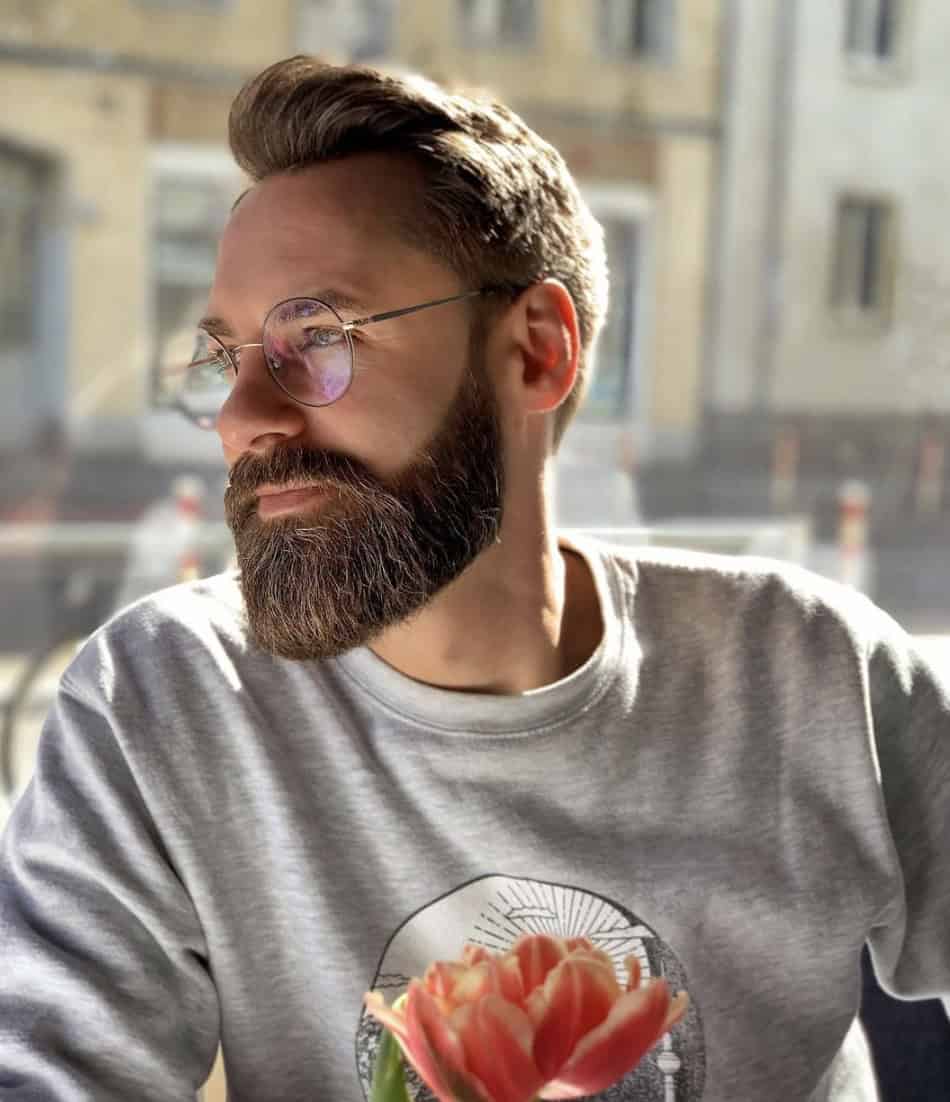 Man with groomed beard in a grey sweater and a flower