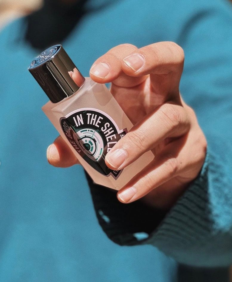 man in a blue sweater holding a bottle of cologne