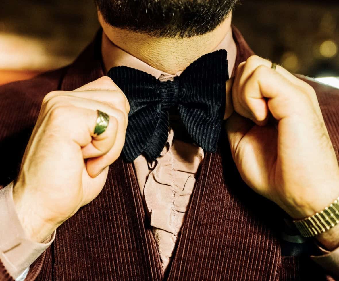 Man in a corduroy suit tightening a bow tie