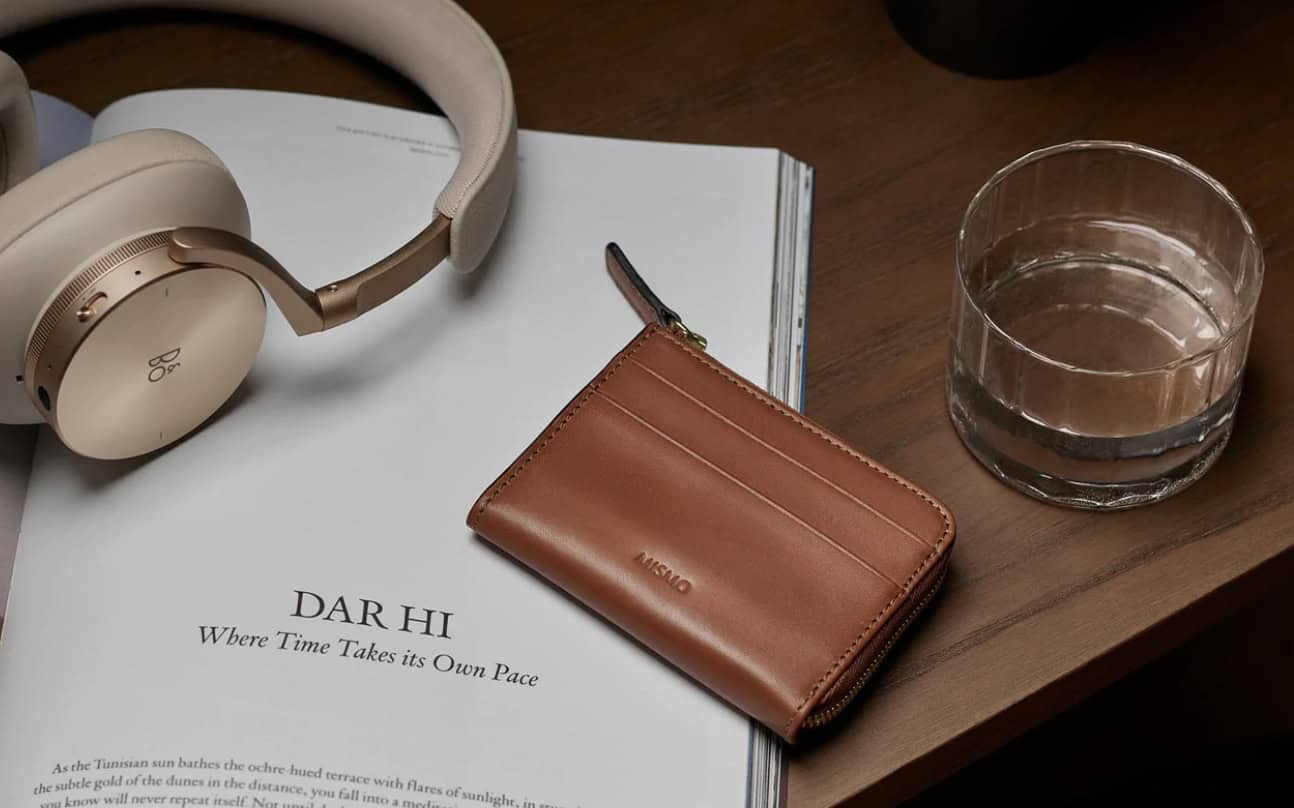 wallet on wood table with headphones, magazine and a drink