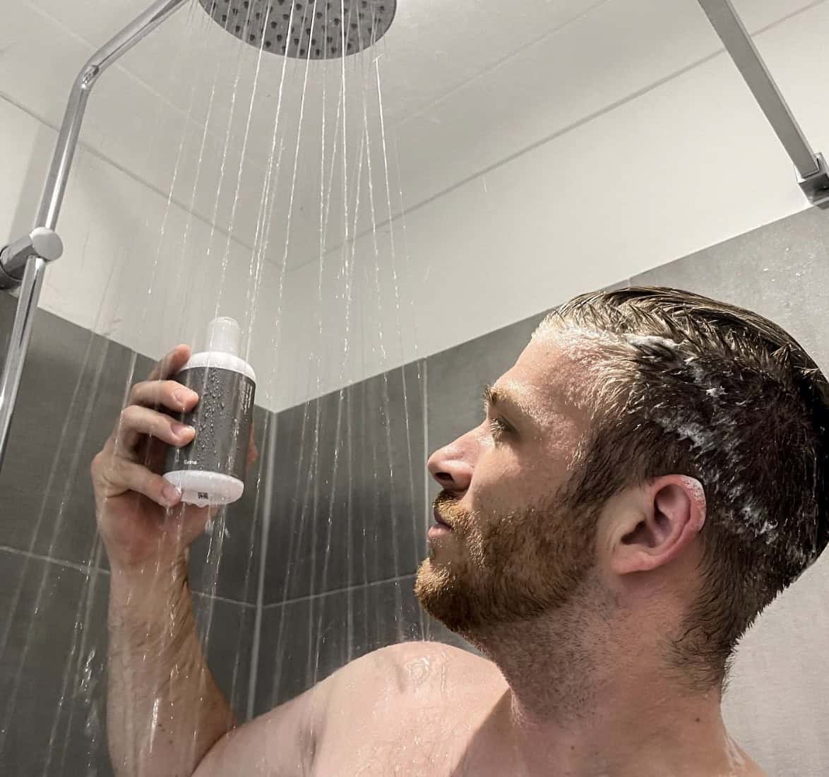 Man in a shower looking at a shampoo bottle
