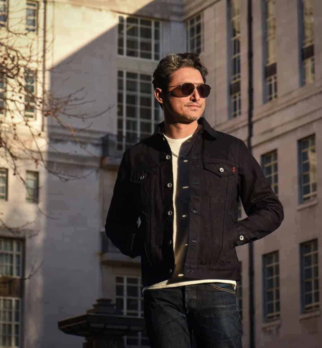 man at sunset wearing sunglasses, jacket and jeans looking away from the camera