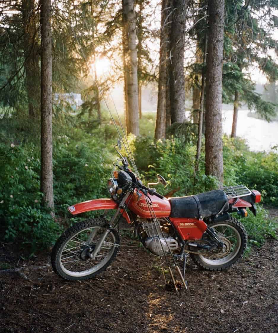 Red dirt bike in the woods with fishing poles leaning against it