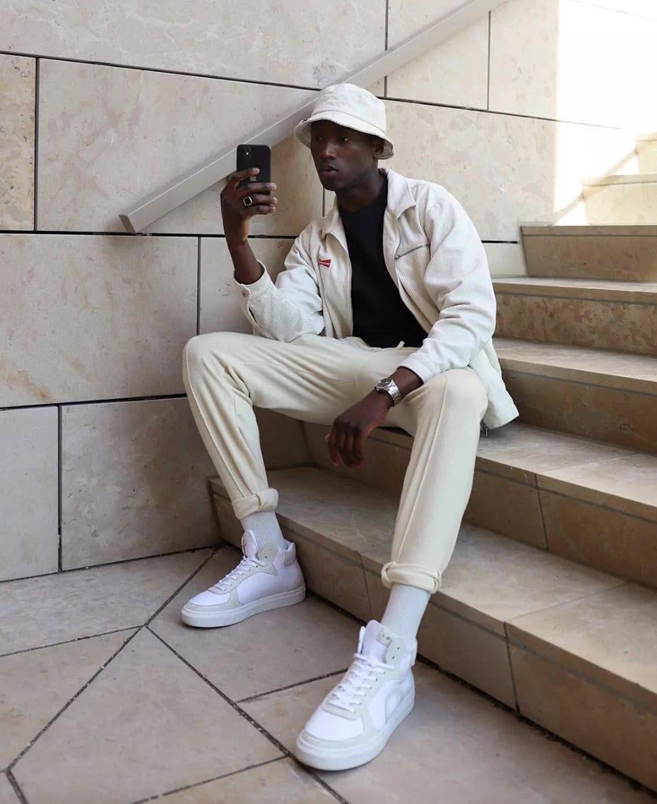 Man sitting on the stairs, wearing a white jacket and pants, looking at phone