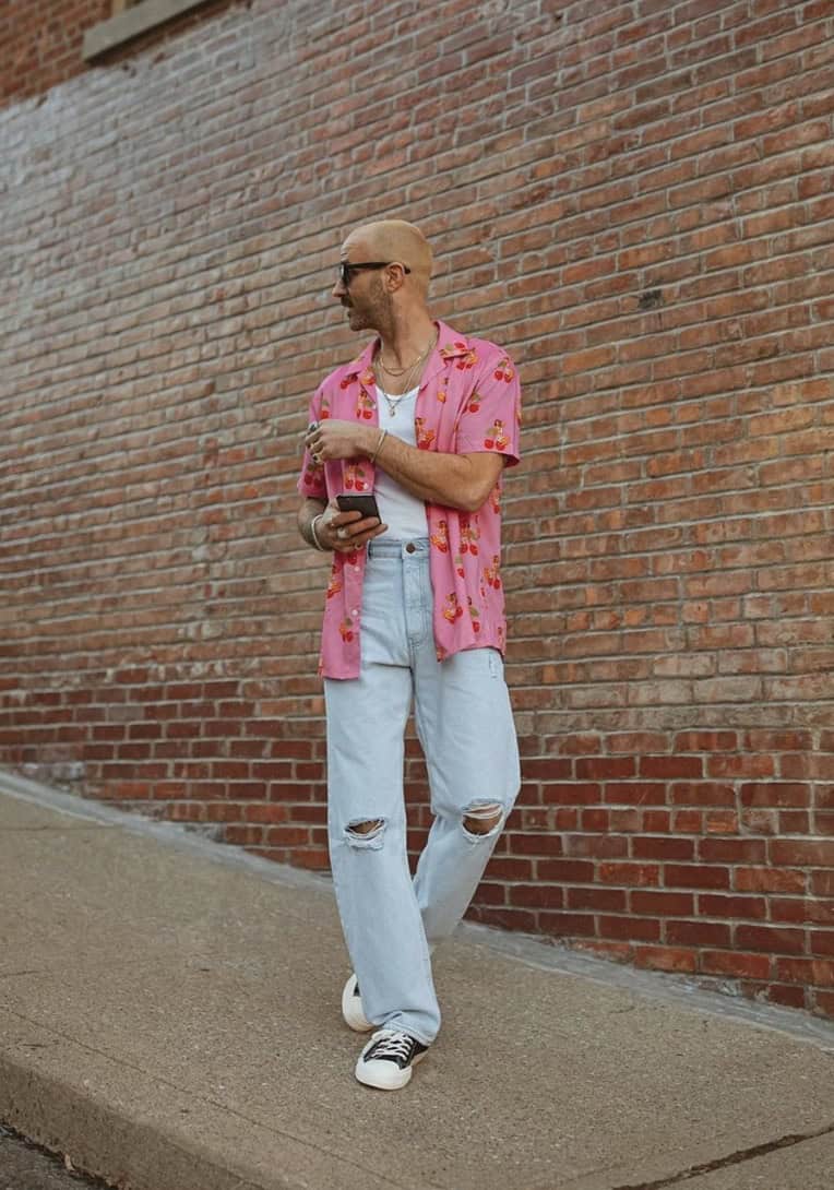 Man looking away from the camera wearing an open pink button-up and ripped jeans