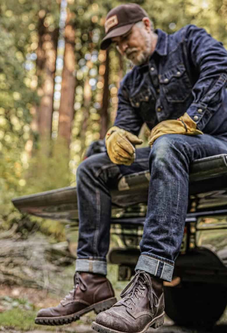 Man sitting on the back of a truck, wearing double denim and Wolverine boots