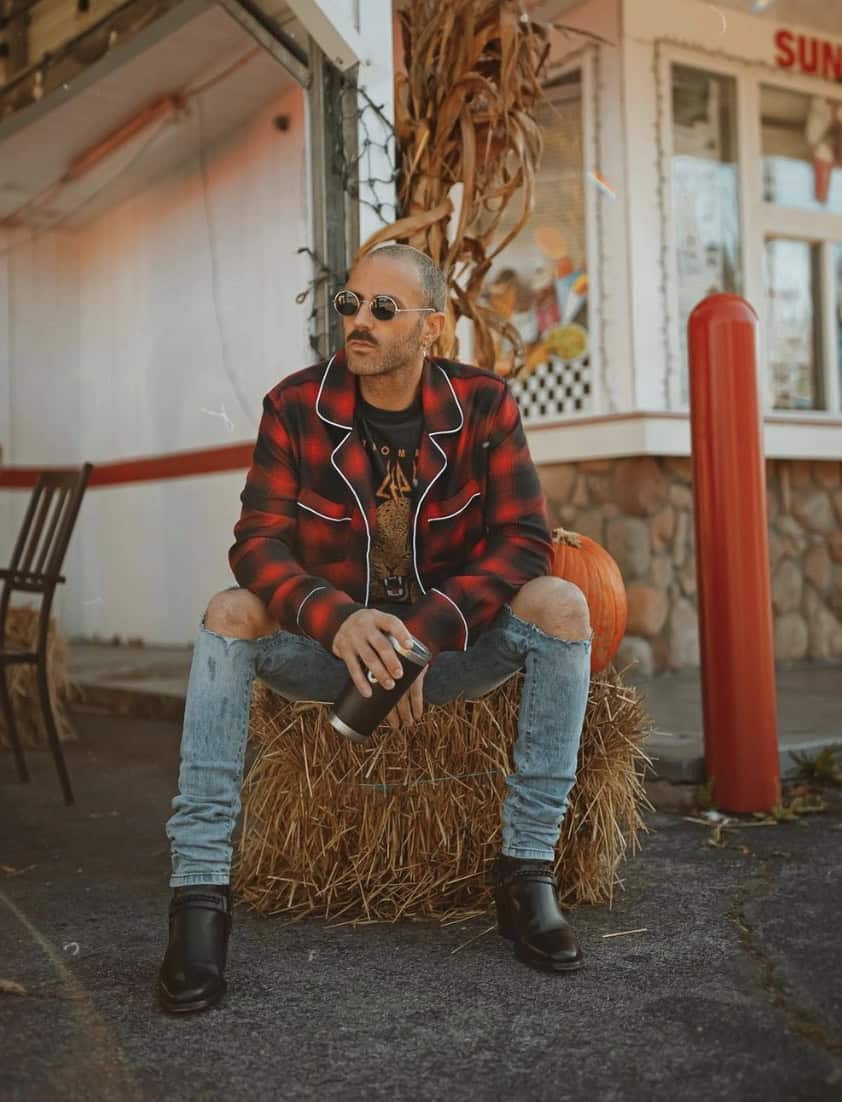 man sitting on a hay bail wearing ripped jeans and plaid shirt