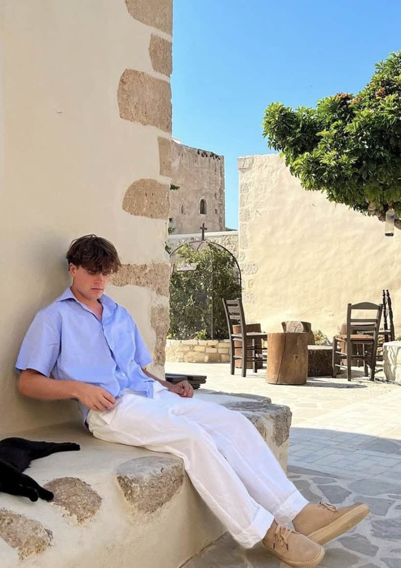 man sitting on a stone bench outside looking at his shoes