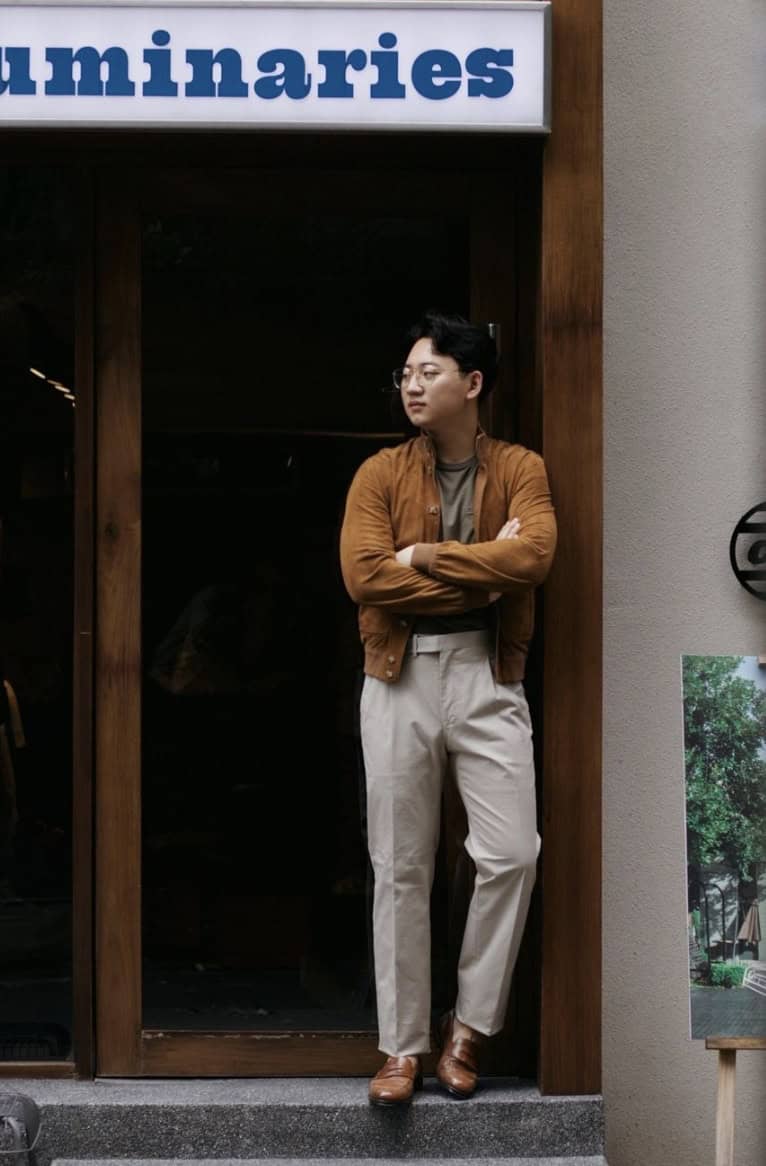 Man standing in a store doorway dressed in trousers, penny loafers, collarless jacket and a turtleneck