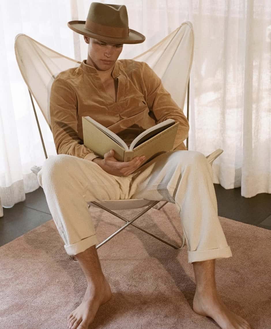 Man wearing a hat sitting in a chair reading a coffee table book