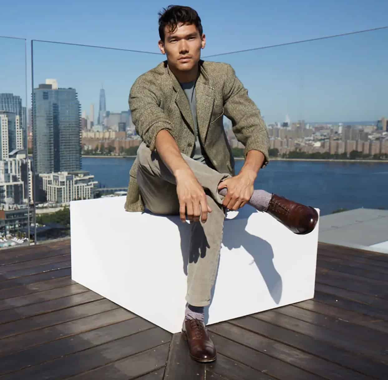 Man sitting on a roof top, skyline behind him in a casual suit and brown dress shoes