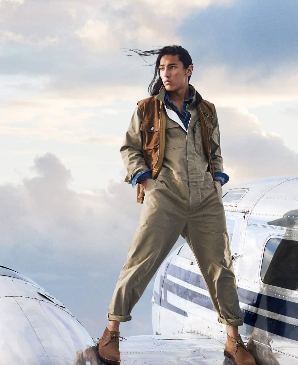man in a jumpsuit standing on the wing of a plane in a jumpsuit