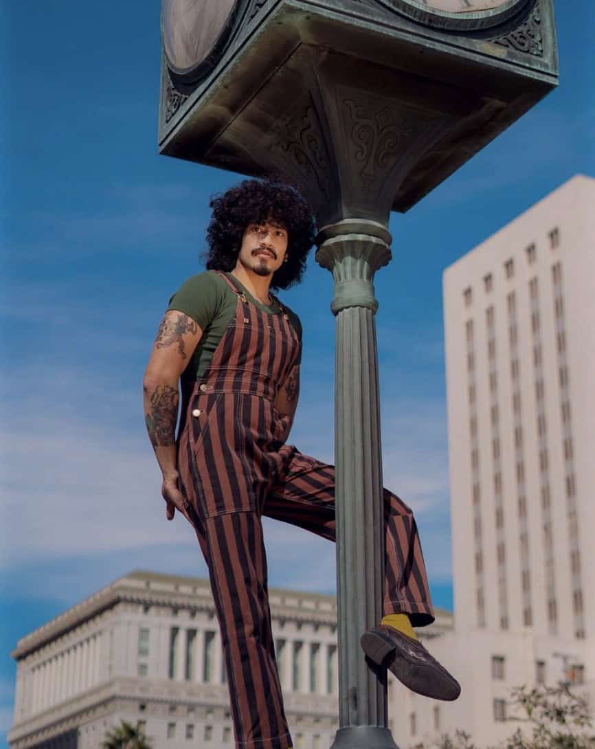 Man hanging off a clock/street lamp in striped overalls