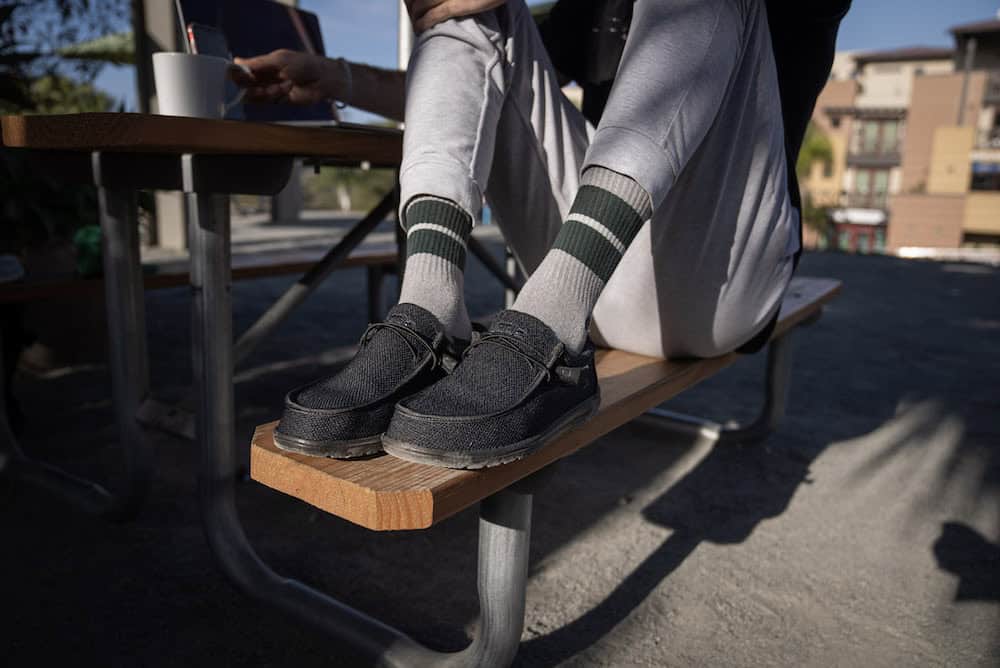 man sitting on bench wearing hey dude shoes