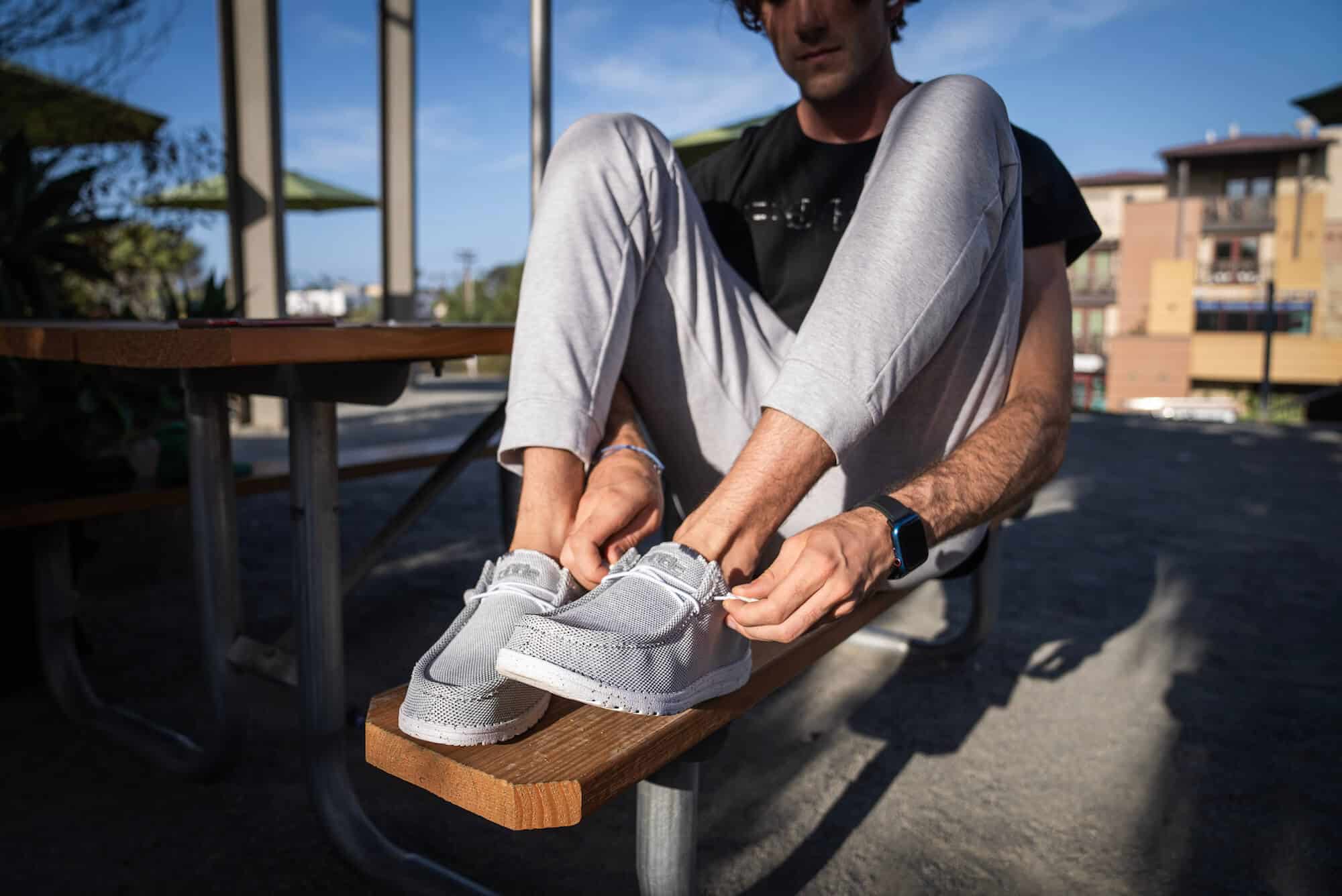 man tightening a pair of hey dude shoes on a bench