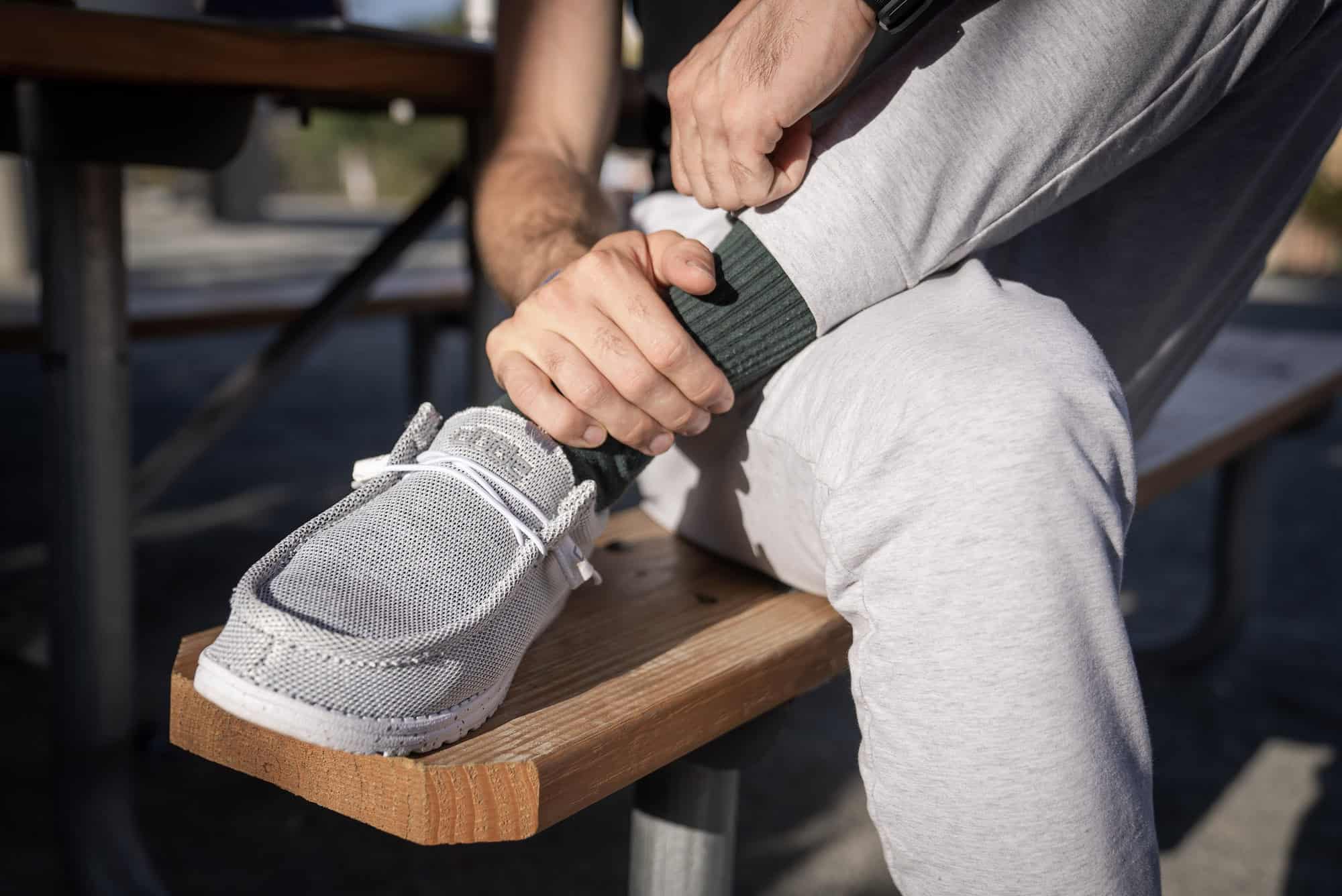 man wearing green socks, holding ankle wearing hey dude shoes