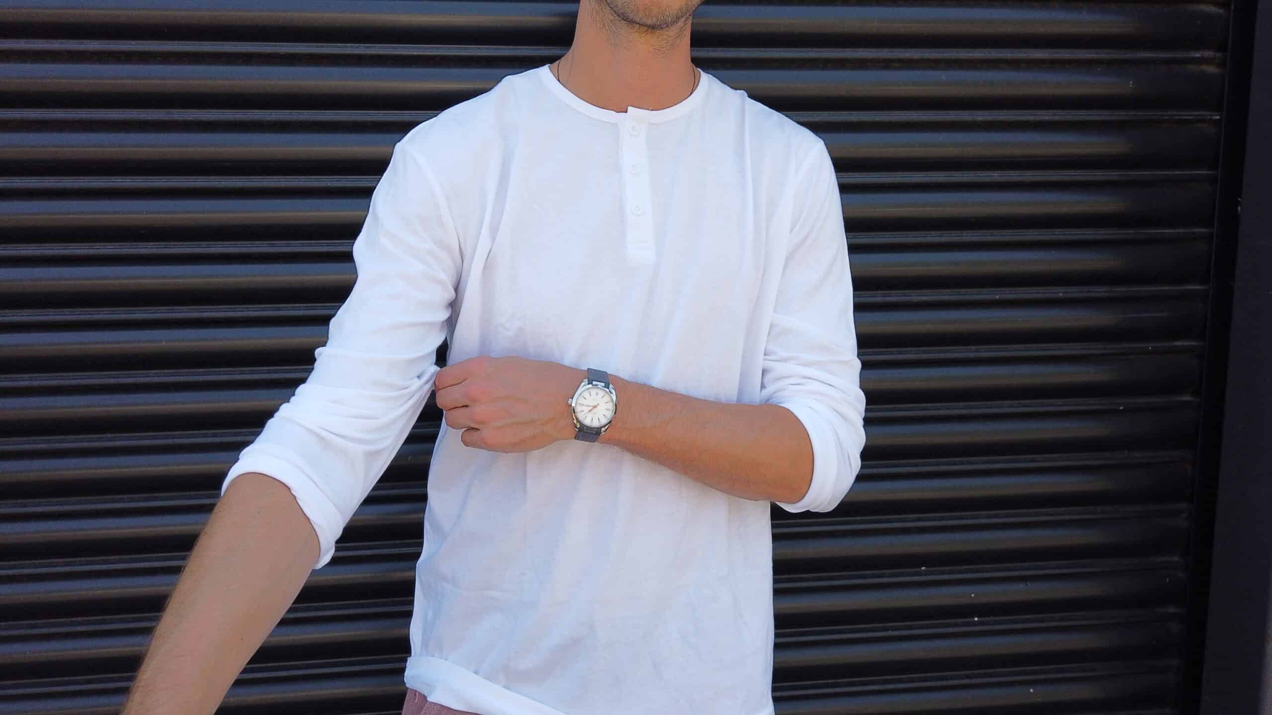 man standing against a garage door rolling up sleeves of a true classic sleeve