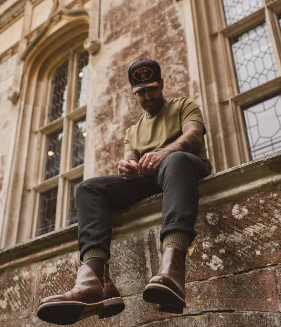 man sitting on ledge wearing a cap, jeans and a t-shirt
