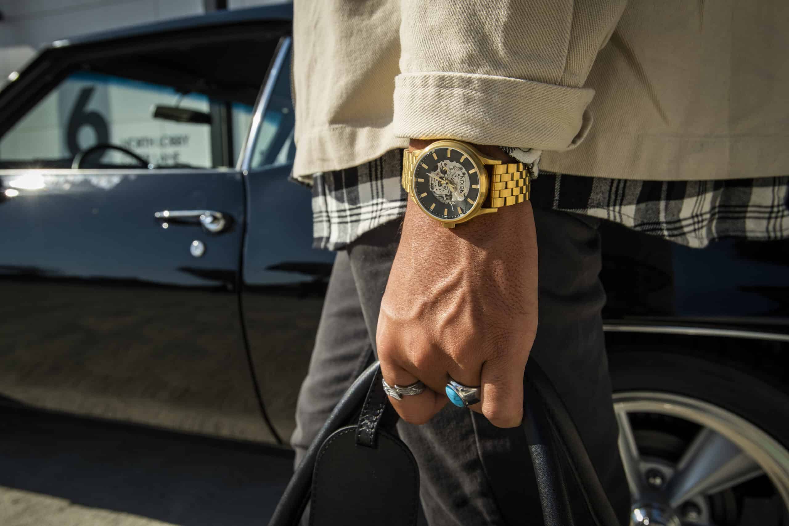 Man walking with a close up on a golf watch, turquoise ring and leather bag