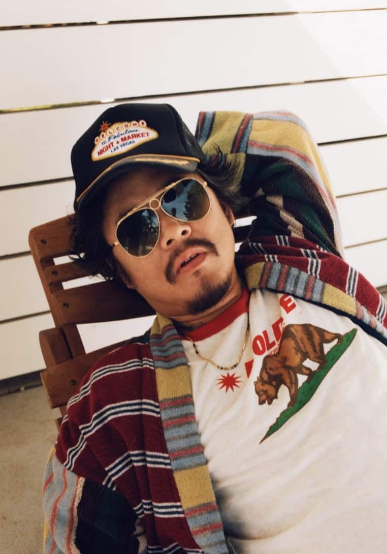 man leaning back on a chair with a hat, sunglasses and chain for men on