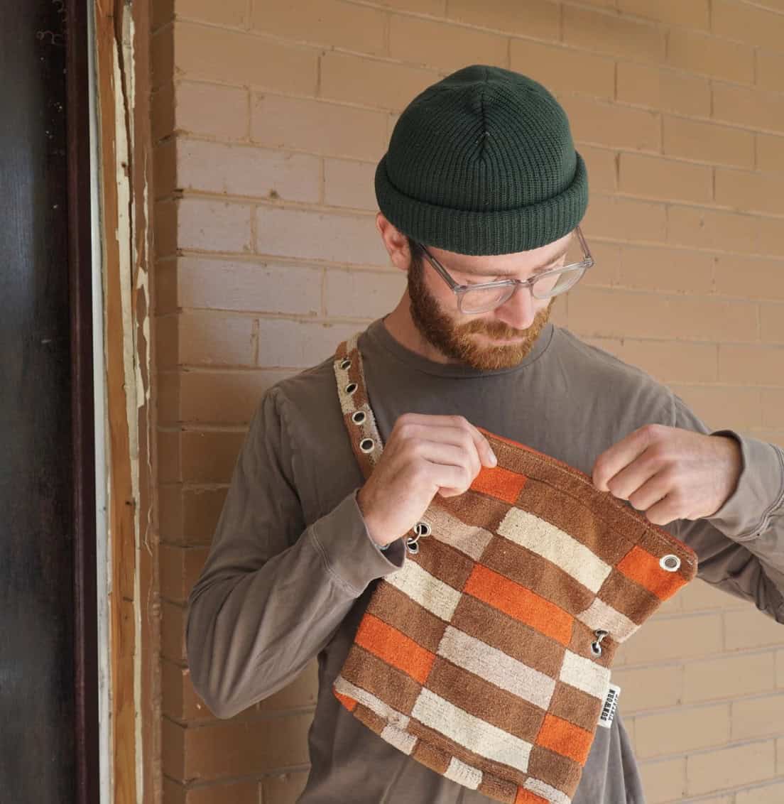 man looking down opening a fanny pack standing in front of a brown brick wall