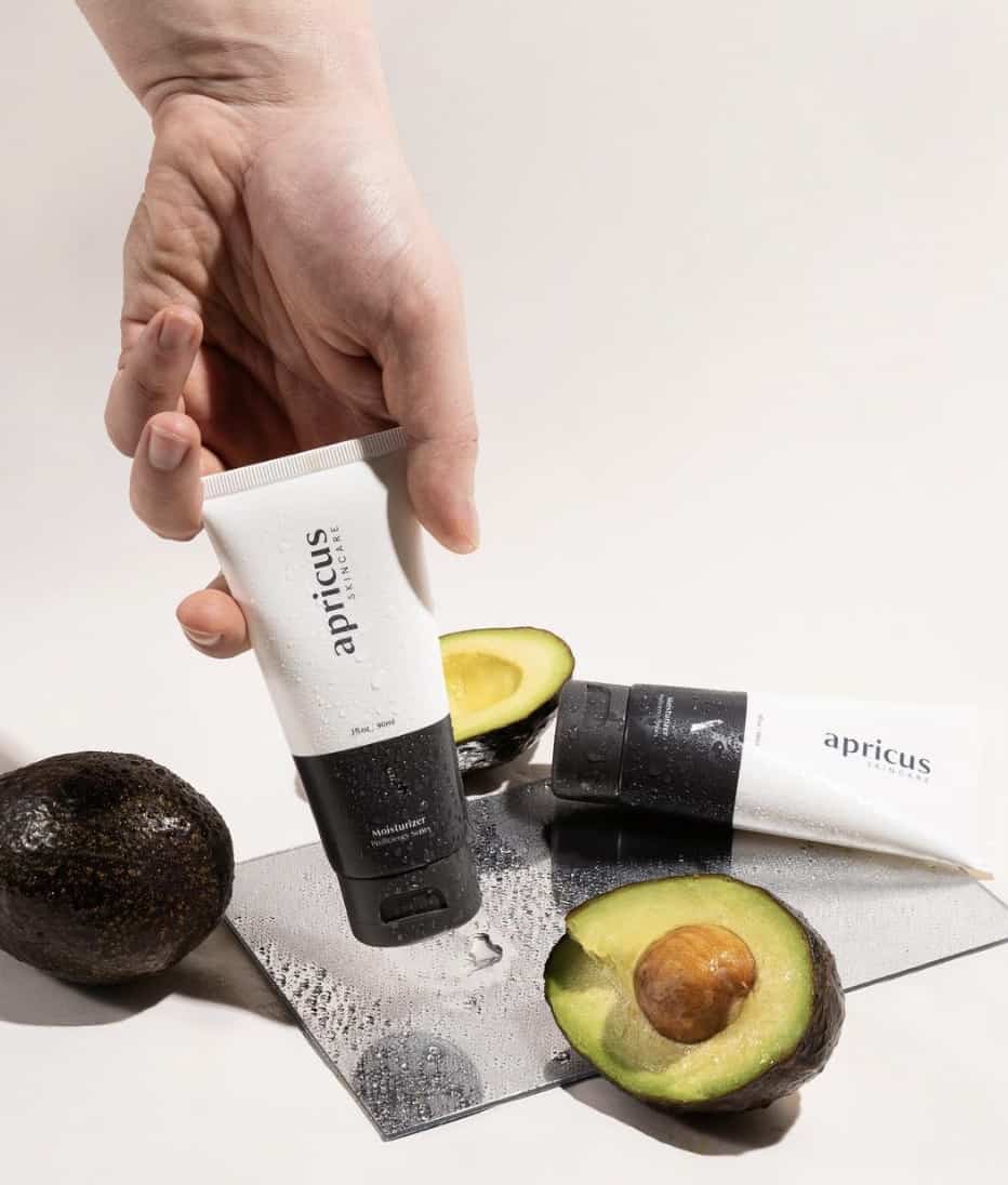 hand holding moisturizer with half cut avocados laying beside