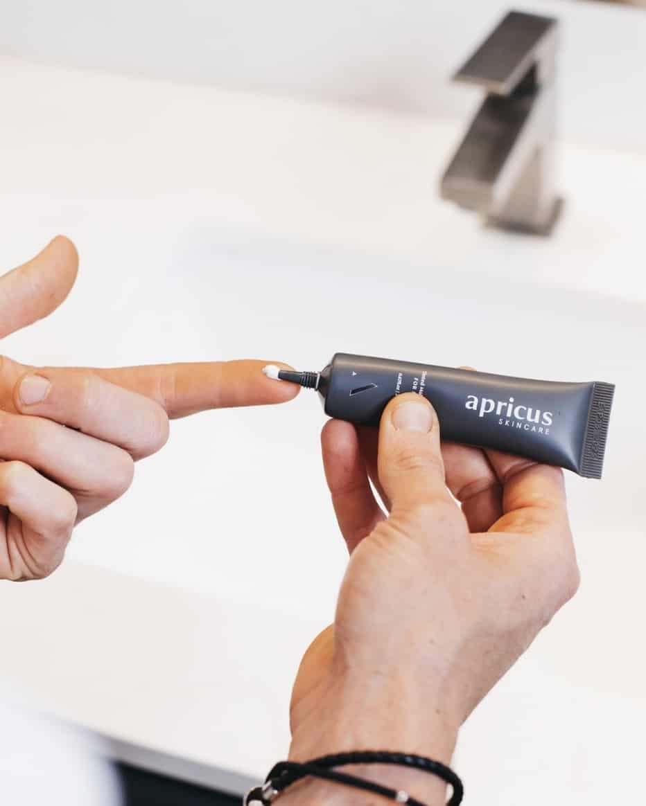 man squeezing tinted moisturizer onto a finger in front of a sink
