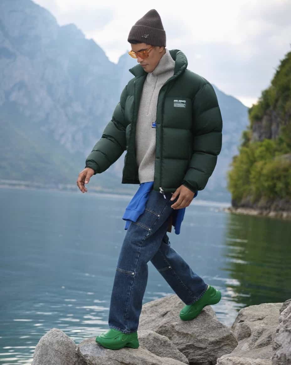 man walking on rocks, with mountains and lakes in the back wearing Axel Arigato 