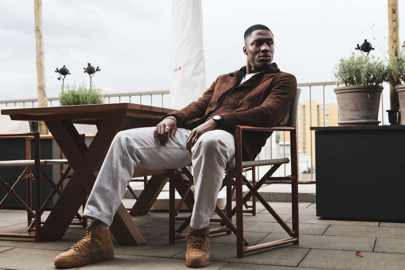 Man sitting outside, wearing a brown suede jacket looking away from the camera 