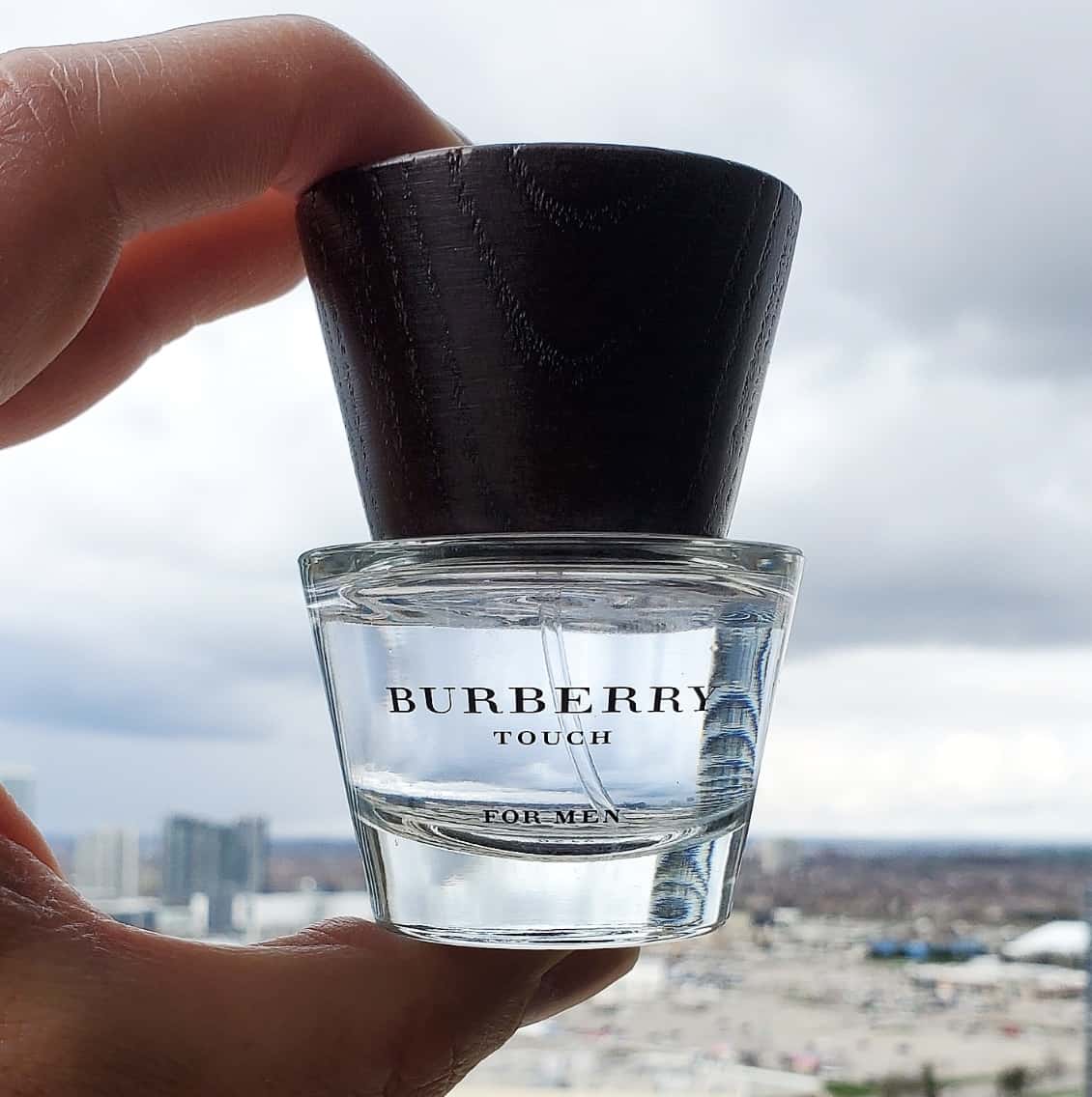 Bottle of Burberry cologne held up to a city skyline