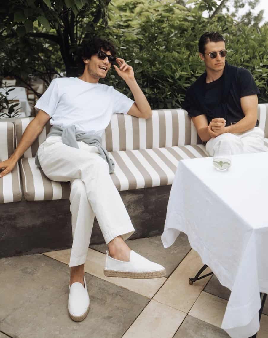 men sitting on a bench outside smiling wearing canvas shoes