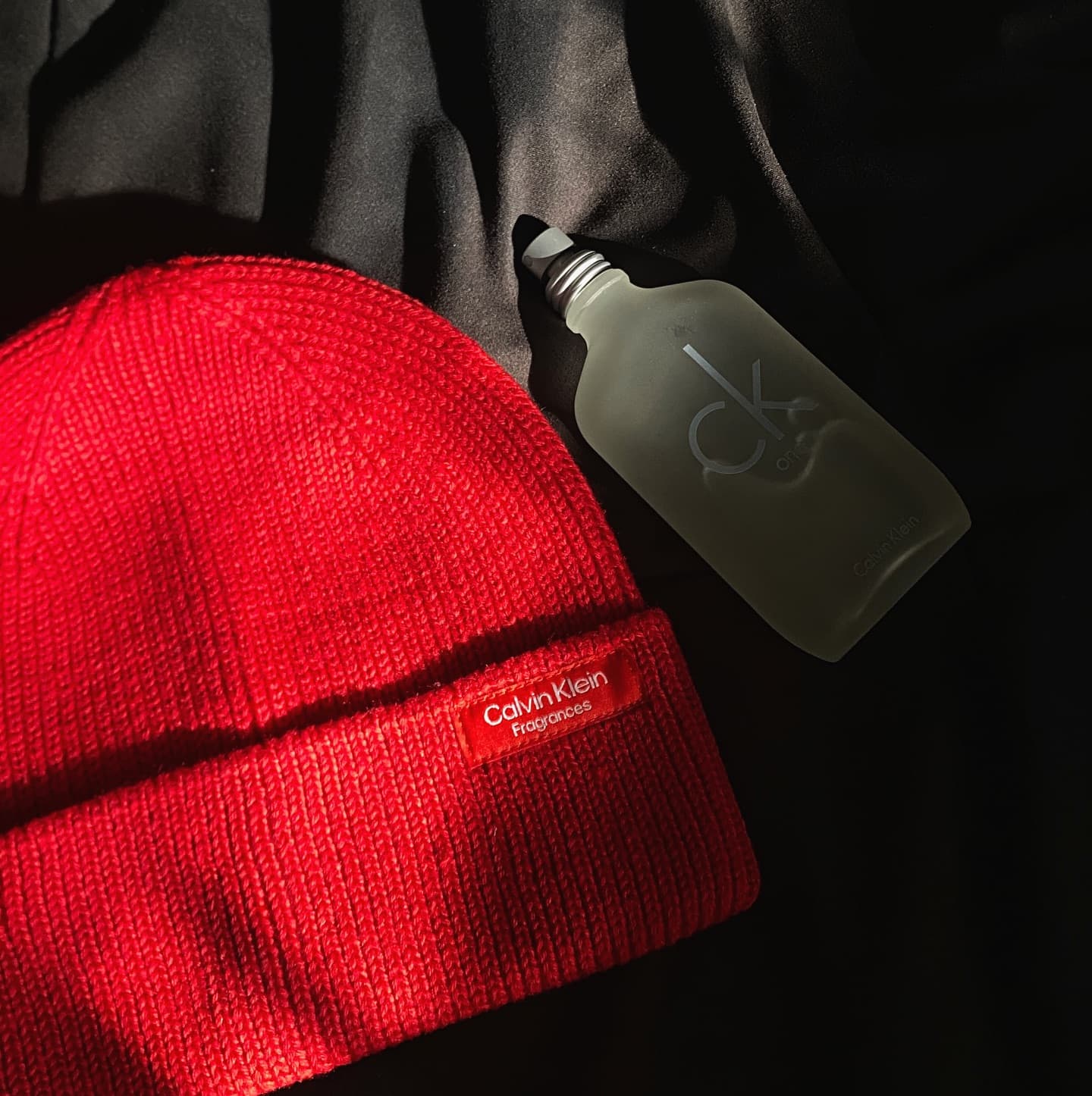a bottle of ck one and a red beanie by calvin klein