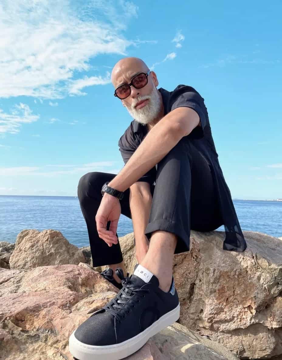 man sitting on rocks by the water showing off Løci sneaker