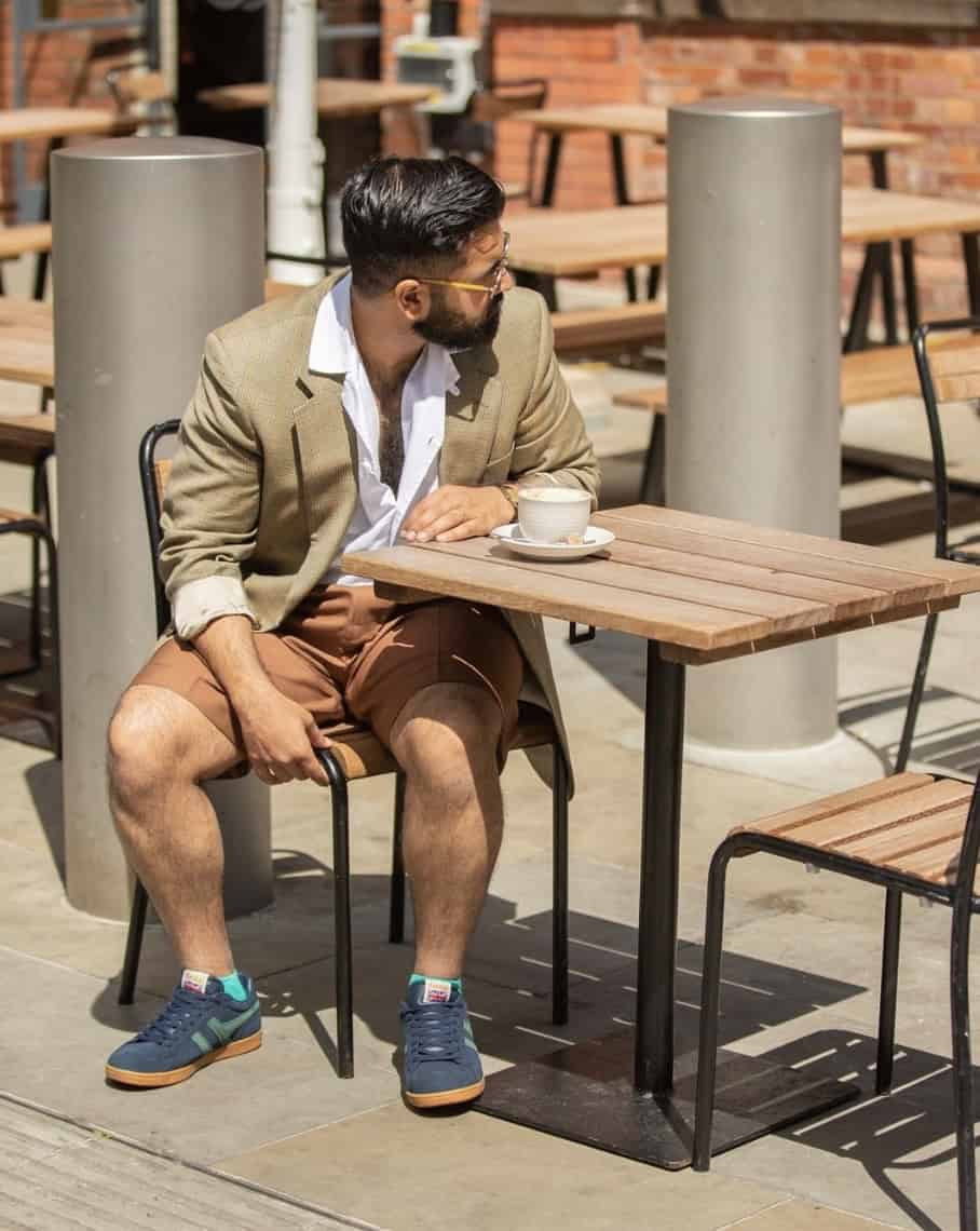 man sitting at table outside wearing a blazer, shorts and sneakers