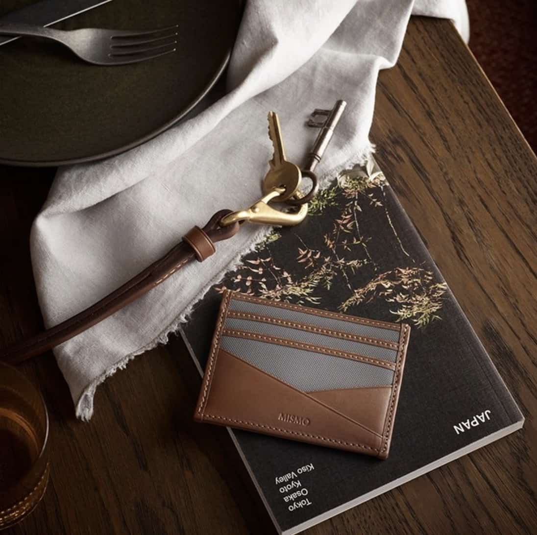leather card holder on top of a magazine with keys next to you