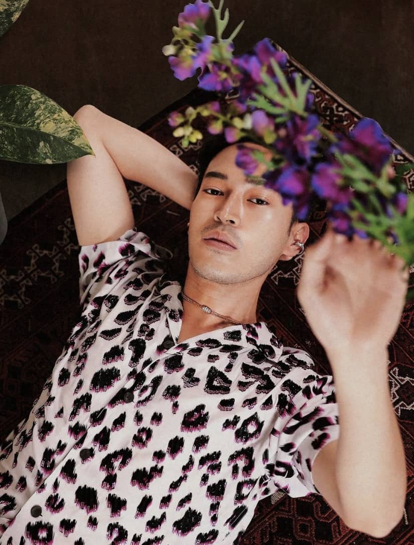 man laying on his back, reaching up to some flowers