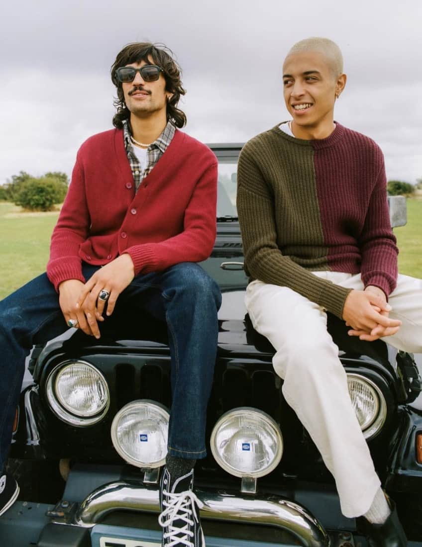 two men sitting on the hood of a black jeep, smiling 