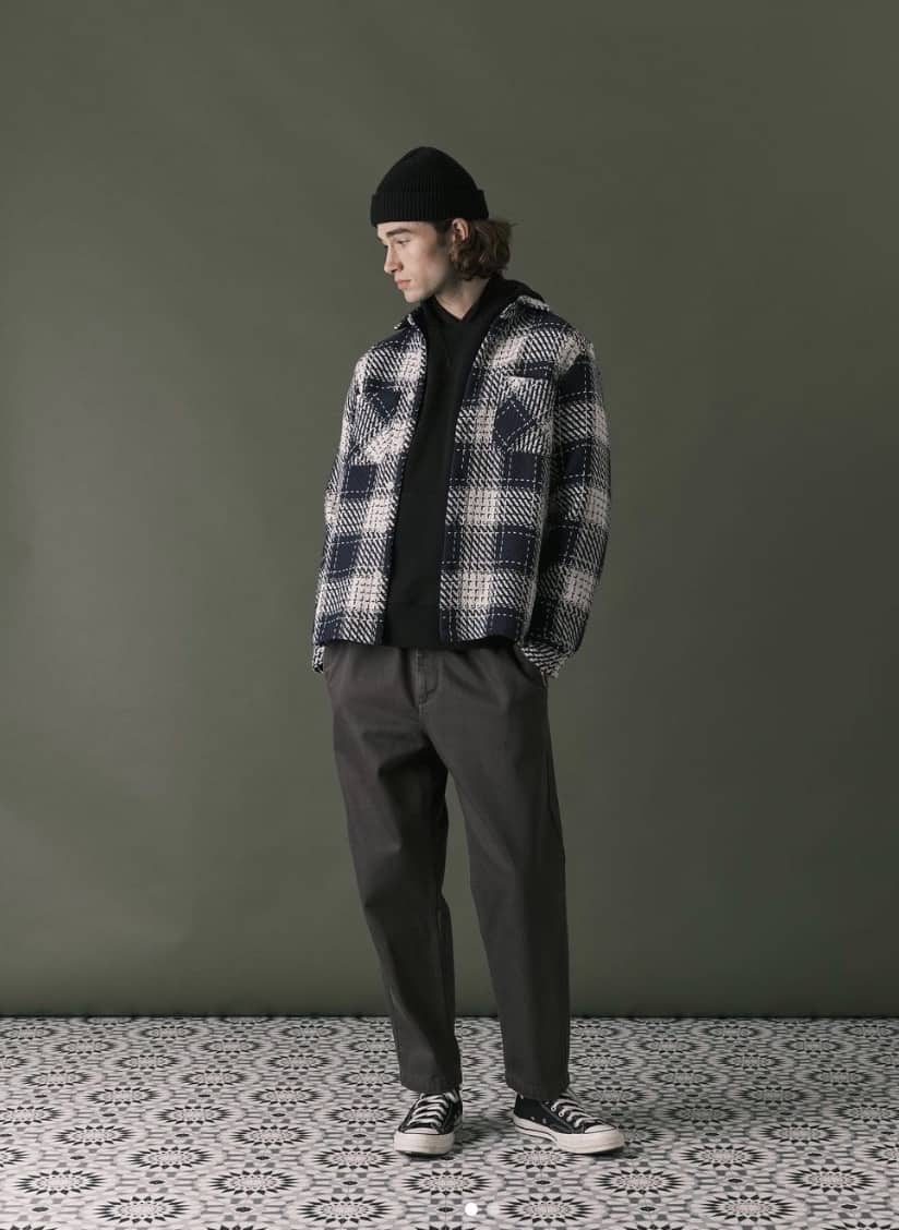 man wearing a flannel and trousers against a green wall and tile floor
