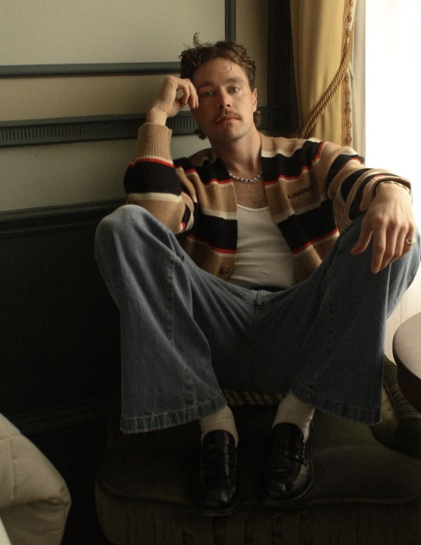 man sitting in a chair, leaning on his hand with his feet up, lighting is dark