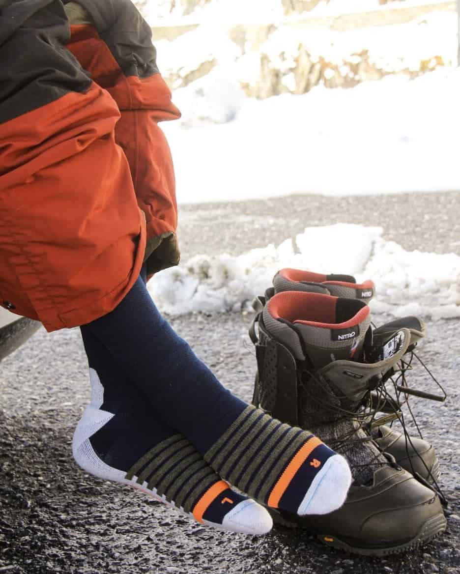 showing a persons feet in ski socks, with boots on the ground next to them, sitting in the trunk of a vehicle 