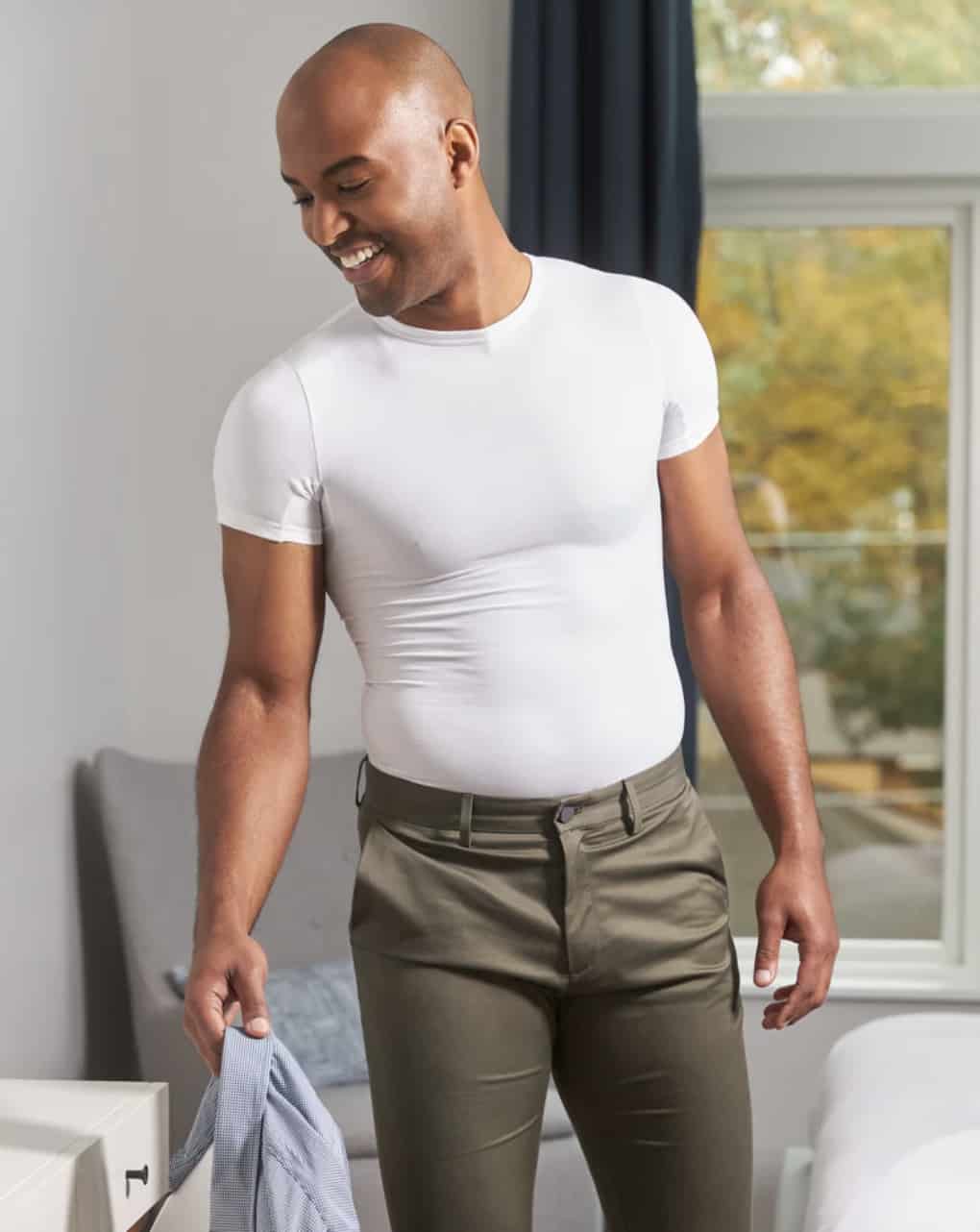 man wearing shapewear, holding a shirt, smiling 