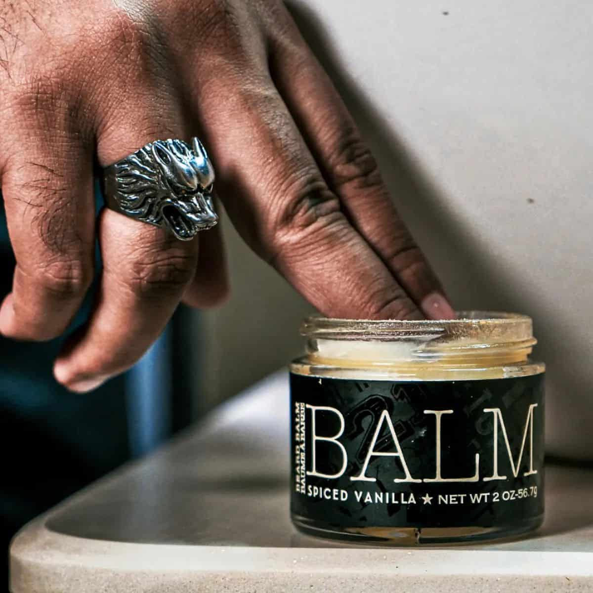 man dipping his fingers into a beard balm container