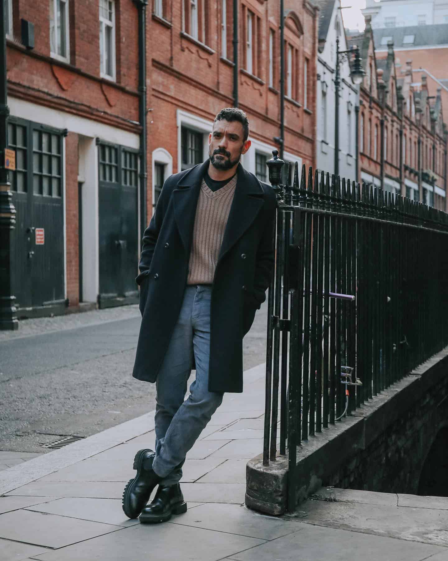 man in a coat leaning at a metal fence