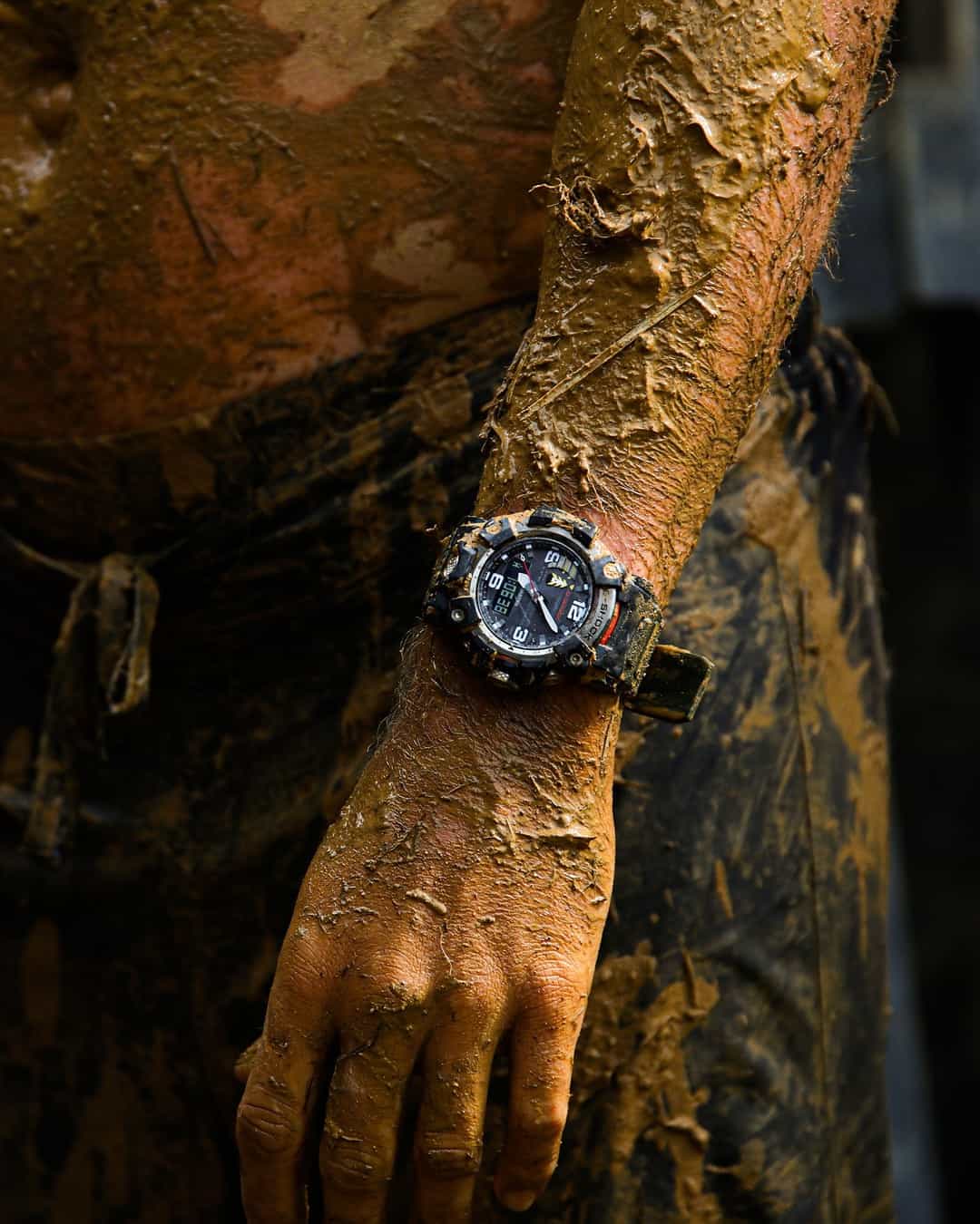 man and his watch covered in mud