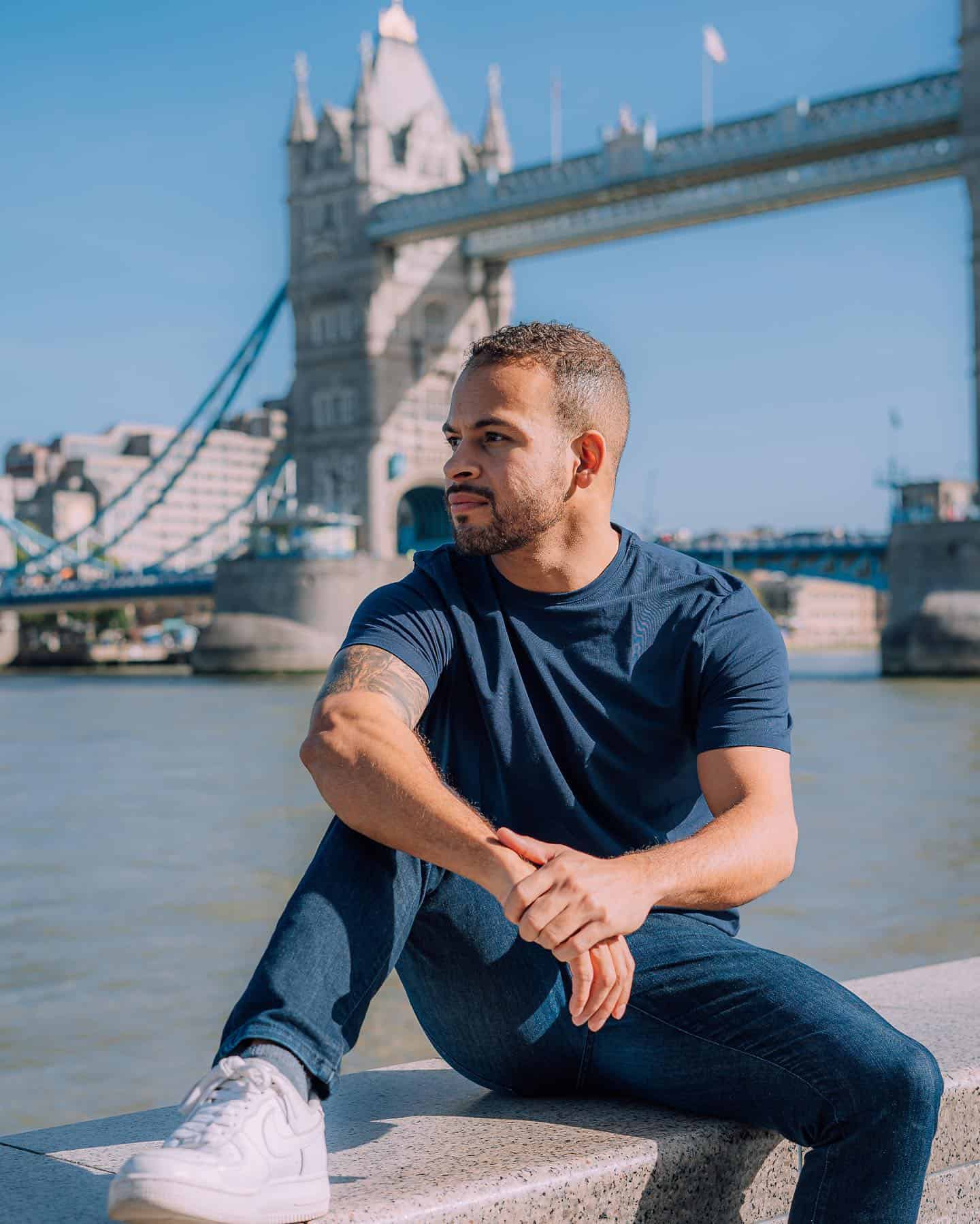 man sitting on a concrete bench in front of the London bridge