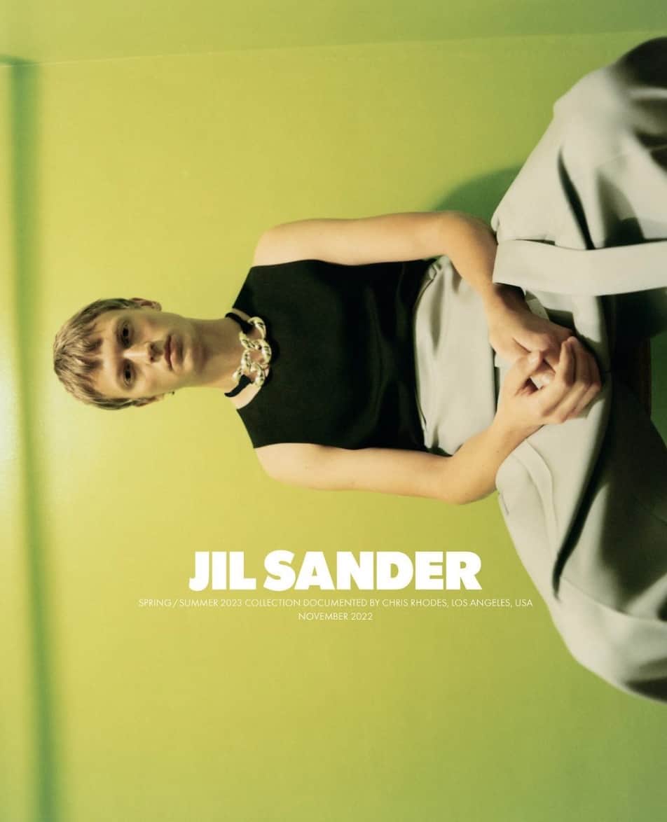 photo of a model sitting against a bright green wall, photo is turned sideways