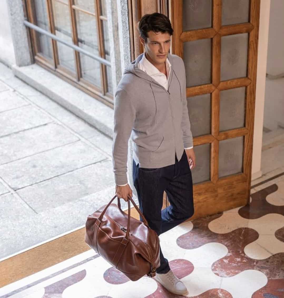 Man walking into a house with a leather duffle bag