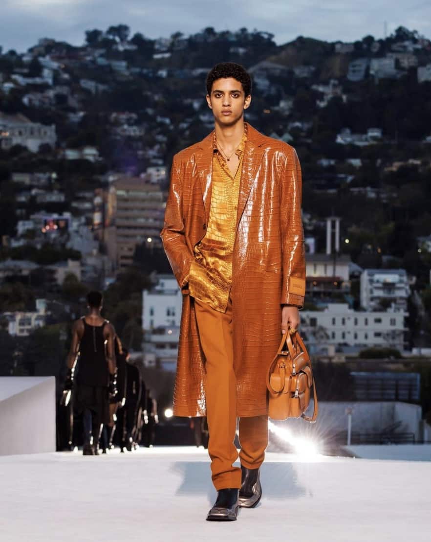 Man in a orange leather outfit walking on a runway